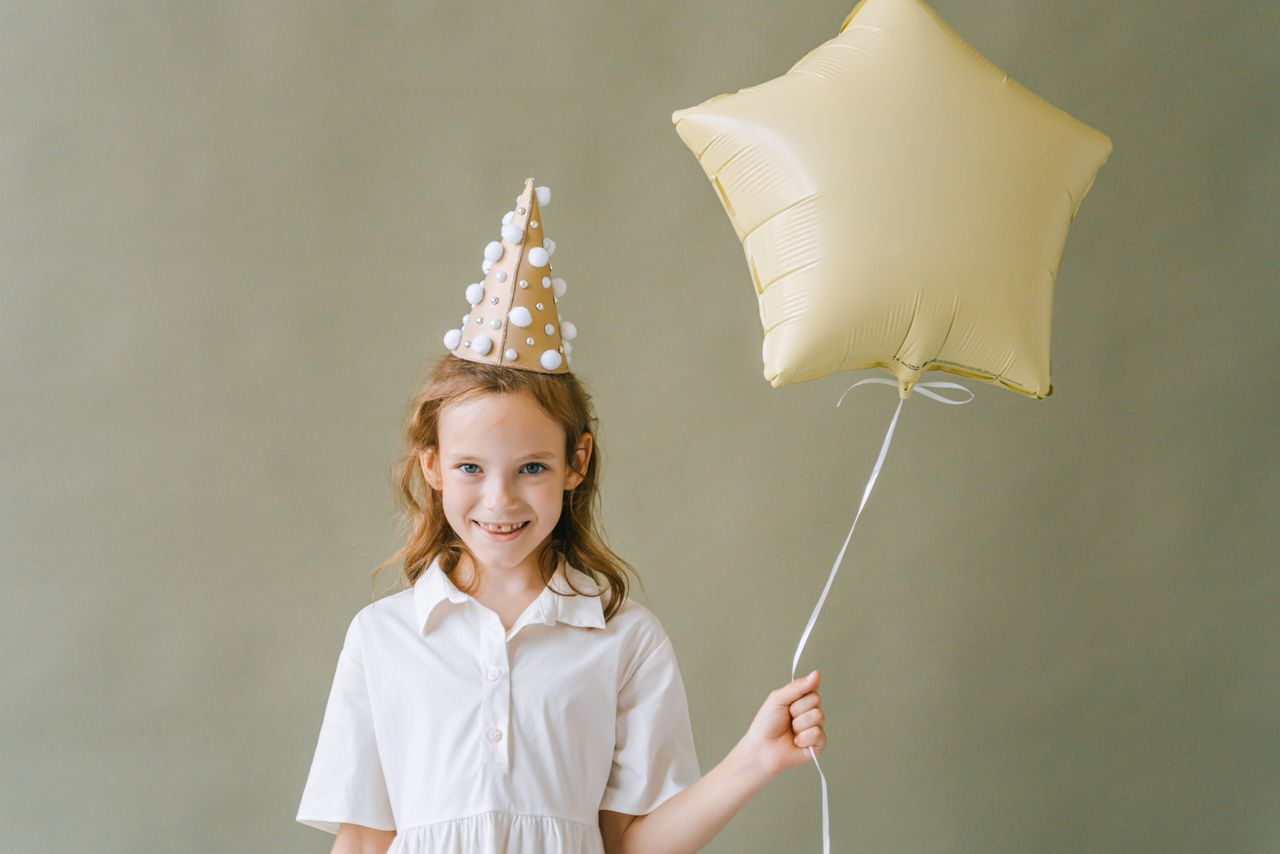 Smiling girl with party hat and star balloon, enjoying a fun birthday celebration.
